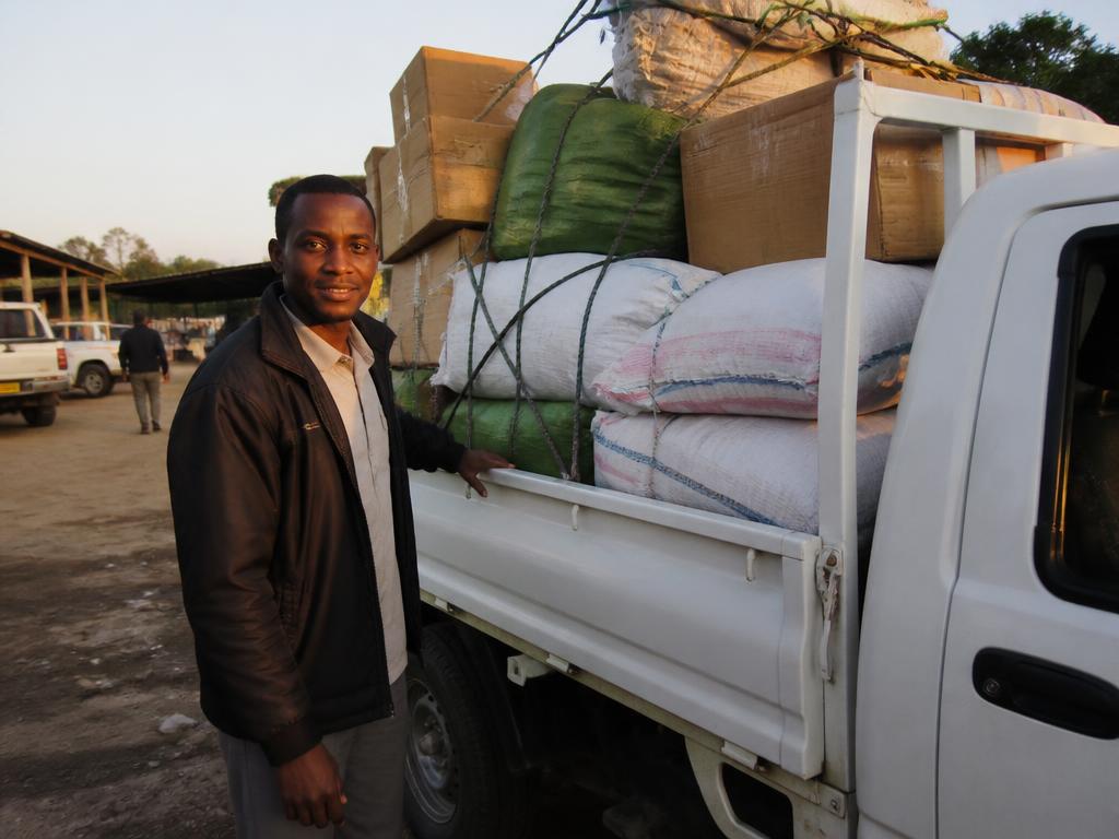 African transporter standing beside a pickup truck loaded with goods for delivery